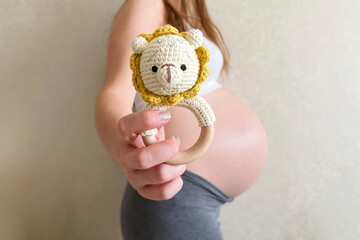 A pregnant girl holds out a knitted rattle in the form of a lion to the camera. Selective focus