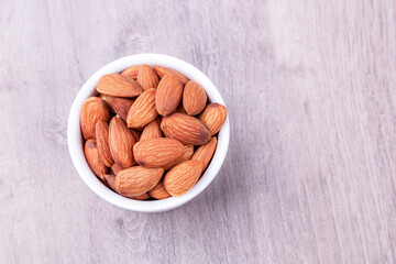 Almonds in white porcelain bowl on wooden table. Almond concept with copy space.
