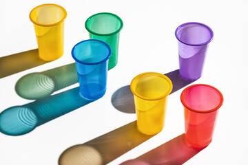 Set of multi-colored plastic cups on a white background. Long shadows, studio shot.