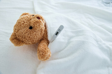 Teddy bear in bed with thermometer and bandage