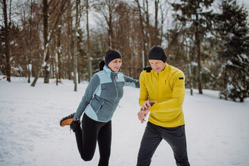 Senior couple warming-up, checking smartwatch in snowy forest before winter hike.