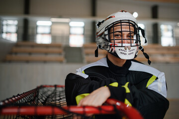 Close-up of woman floorball goalkeeper in helmet concetrating on game in gym.