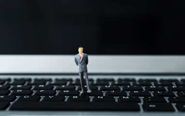 Miniature businessman standing on laptop keyboard