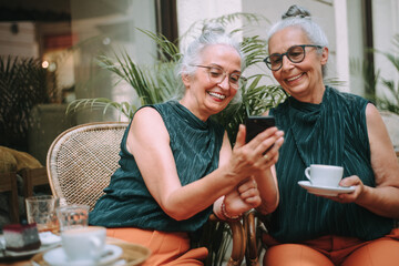 Happy senior women twins having coffee break in city, smiling and talking. - obrazy, fototapety, plakaty