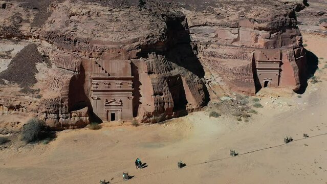 Aerial view of tourists in front of tombs at the Archaeological Site of Al-Hijr (Madain Salih) in sunny Saudi Arabia - circling, drone shot