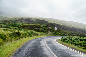 Small narrow asphalt road with bends in a mountains and fog in the background. Dangerous conditions in country side. West of Ireland.
