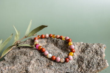 Bracelet made of natural pink agate stones beads on green background. Handmade jewelry. Woman...