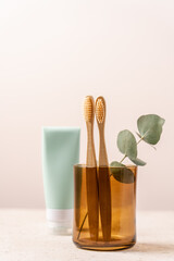 Bamboo toothbrushes in glass and tube of toothpaste on light background. Dental concept