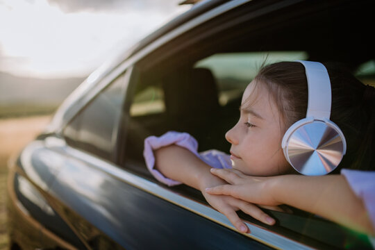 Little girl with headphones looking out of the car window during the ride.