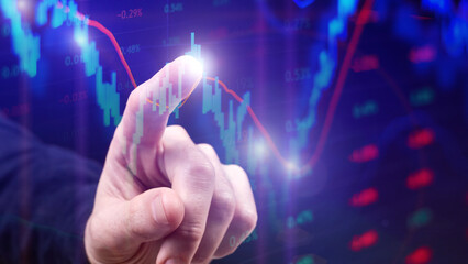 The trader points his finger at the stock chart on the monitor