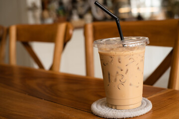 Iced coffee in take away cup (plastic glass) on the wooden cafe table. Disposable transparent plastic coffee cup in coffee shop.