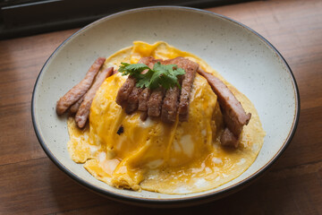 Creamy Omelete with roasted pork on rice in white ceramic dish on wooden table. Thai Asian style food. Selected focus.