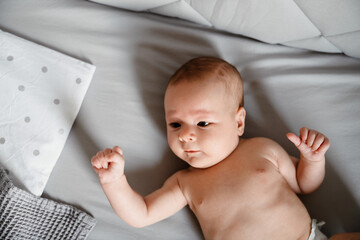 White undressed newborn baby lying in crib with gray linen at bedroom