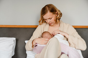 White woman in housecoat breastfeeding her newborn baby in bedroom