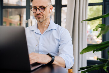 European man in earphones working with laptop while sitting at office