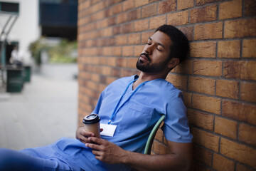 Tired caregiver man resting outdoor, in front of nurishing home.