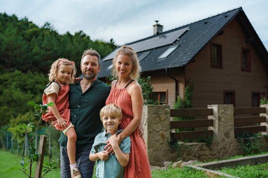 Happy family near their house with solar panels. Alternative energy, saving resources and sustainable lifestyle concept.