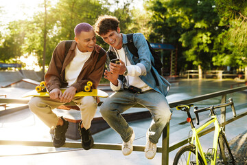 Two young handsome stylish smiling boys with phone watching something