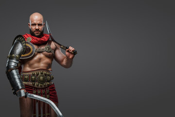 Fototapeta na wymiar Shot of roman gladiator from ancient rome dressed in armor and cloak against gray background.
