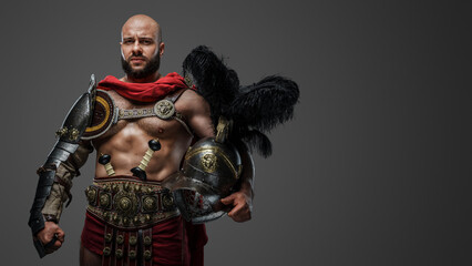 Obraz premium Shot of serious roman gladiator with naked torso and plumed helmet isolated on grey background.