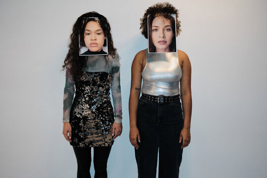 Horizontal medium long studio shot of two young women covering their own faces with portraits of each other, self-identity concept