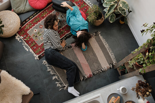 Top-down shot of ethnically diverse young women wearing stylish casual clothes relaxing on floor in living room at home talking about something