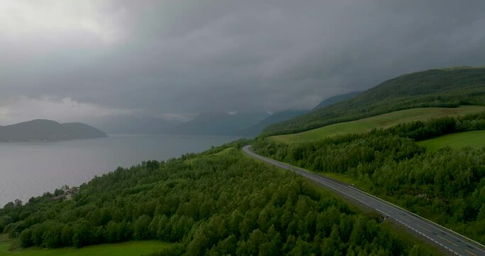 Following E8 highway into dark clouds, fog, rain. Norway. Aerial, drone.