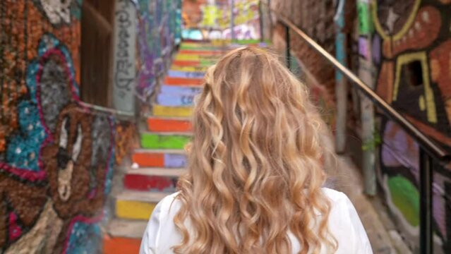 Close up of a young blonde girl on her back turning to camera in urban painted alleyway 