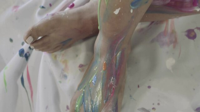 Close up of a woman's feet and legs, covered in fresh colorful paint all over her body