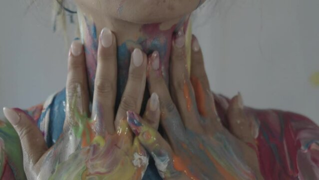 Woman's hands moving down from her neck mixing fresh colorful paint over her body
