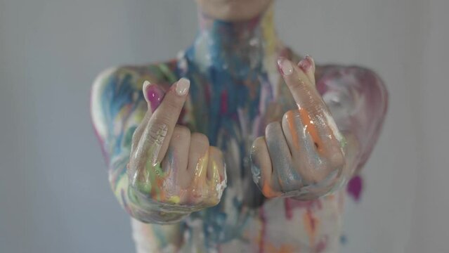 Close up of a woman's hands making finger hearts, covered in fresh colorful paint all over her body. Korean hand gesture for hearts.