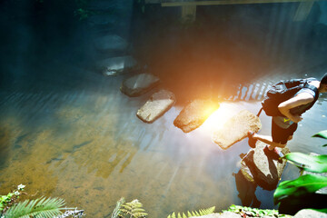 Male hiker with backpack crossing a river on stones