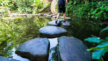 Male hiker with backpack crossing a river on stones
