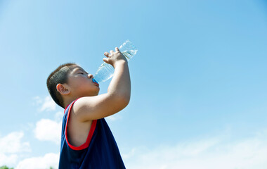 Little asian boy drinking water against blue sky