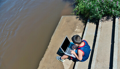 Little boy with laptop on the lake shore