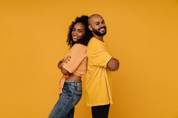 Black young man and woman smiling while standing back to back