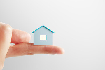 Fototapeta na wymiar Mortgage and bank loan concept with small blue house layout on human finger on light background