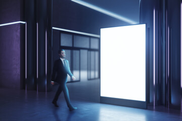 Walking businessman by blank white illuminated board with place for your logo or text in dark empty...