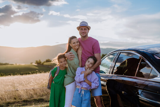 Happy Family On Car Trip Having Break In Nature, Next Their Electric Car.