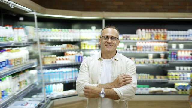 Portrait of a middle-aged man in glasses in a store against the background of dairy products. Store interior