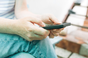 Casual female person wearing jeans trousers using smartphone device outdoors while sitting on the bench in house back yard