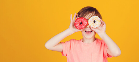 Happy child played with donuts on yellow background wall. Kid enjoying sweets. Cute funny boy...
