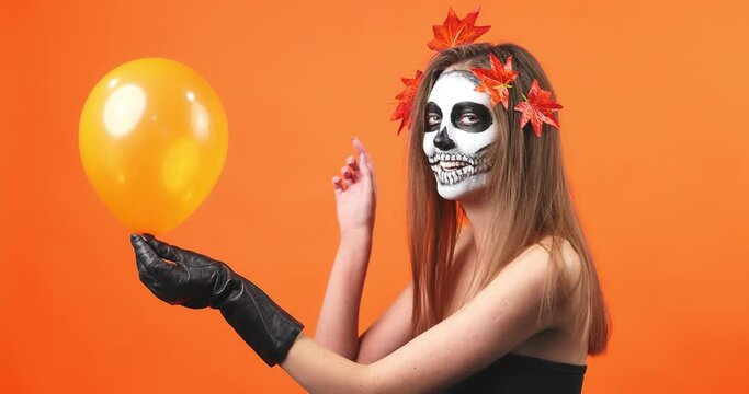 Beautiful makeup style for Halloween. Brunette model wears skull makeup and pops a balloon.