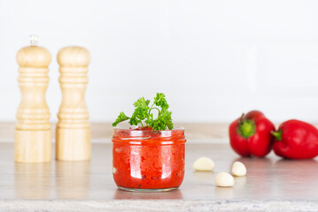 Vegetable salad ajvar in a glass jar for the winter: sweet peppers, eggplant, tomatoes, spices, garlic, parsley on the kitchen table.