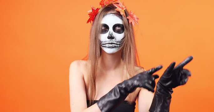 Woman in the image of death Santa Muerte or sugar Mexican skull on a orange background. Halloween makeup.
