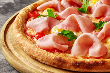 Closeup of pizza with melted mozzarella, ham, quail eggs, tomatoes and fresh greens on wooden board