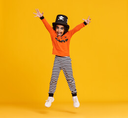 Happy ethnic boy in pumpkin costume   jumping and celebrates Halloween on yellow background