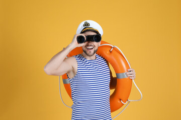 Sailor with orange ring buoy looking through binoculars on yellow background