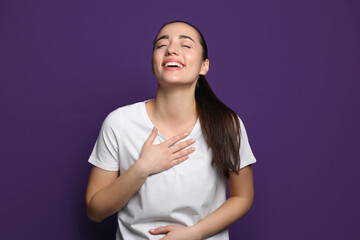 Beautiful young woman laughing on purple background. Funny joke