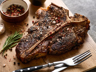 Grilled T-Bone Steak with salt and pepper  on cutting board on dark grey background. Roasted T-Bone...